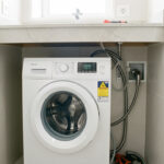 Lave-linge blanc installé dans une salle de bain moderne avec une plomberie discrètement dissimulée dans le mur.