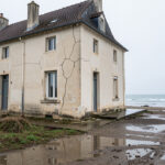 Maison ancienne près du littoral d’Oléron, avec des fissures visibles sur une façade claire et un sol humide après la pluie.